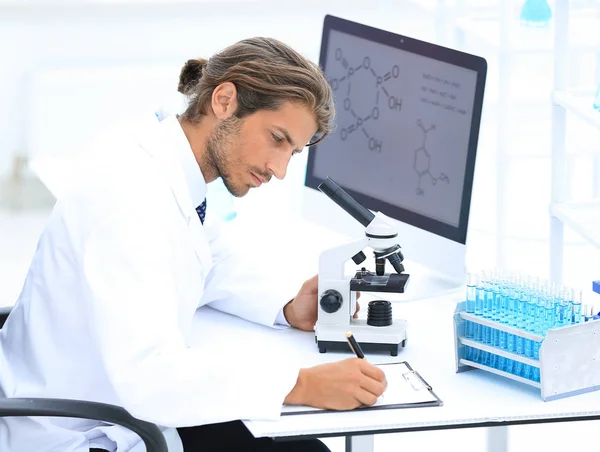 Працівник лабораторії сидить за столом з мікроскопом — стокове фото