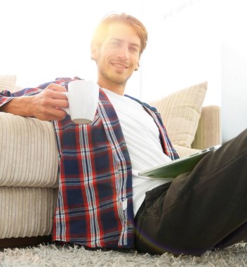 genç adam kanepede yakın katta oturan bir fincan tutan dizüstü bilgisayar ile