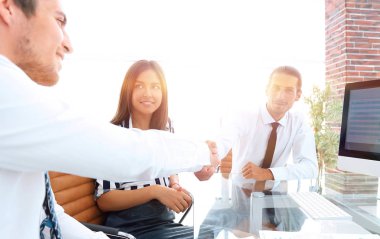 Erkekler masada otururken el sıkışıyor ve gülümsüyor.