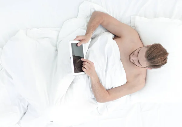 Усміхнений чоловік за допомогою цифрового планшета лежить на ліжку — стокове фото
