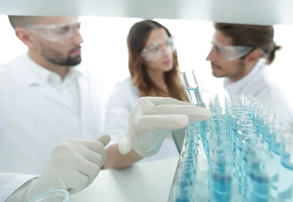 Background image is a group of scientists studying the liquid in the glass tube. — Stock Photo, Image