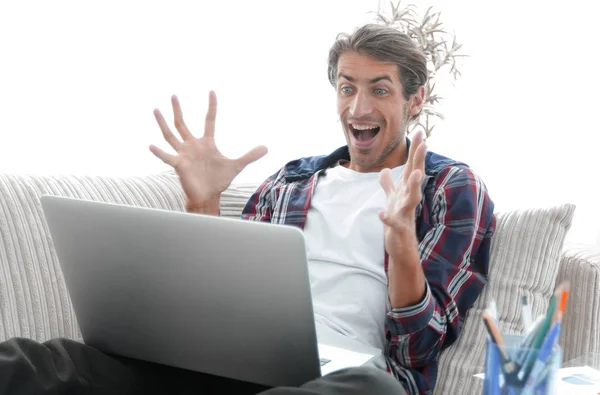 Jovem surpreso com laptop sentado no sofá — Fotografia de Stock