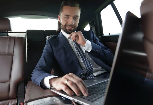 Hombre de negocios lee información sobre el ordenador portátil mientras está sentado en el coche —  Fotos de Stock