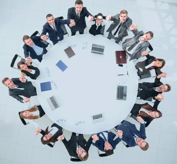 Directeur en business team zitten aan de ronde tafel en houden elkaars handen vast. — Stockfoto