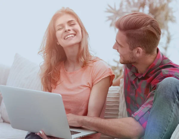 Jong paar is met behulp van een laptop en glimlachend zittend op de Bank thuis — Stockfoto