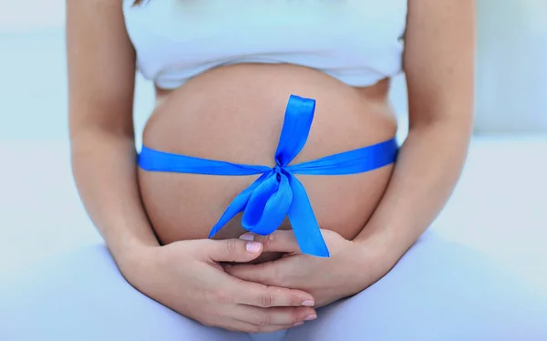 Крупним планом вагітна жінка зав'язує на животі блакитну стрічку — стокове фото