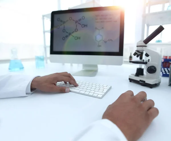 A scientist uses a computer and a microscope — Stock Photo, Image