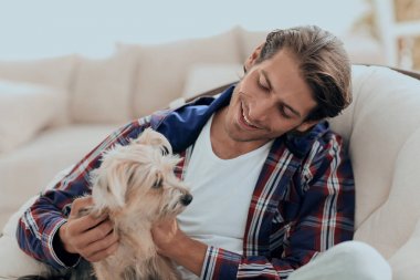 yakışıklı olan büyük bir koltukta otururken köpeğini okşayarak.