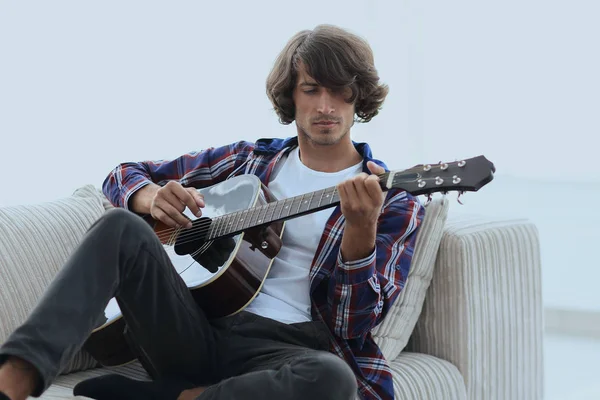 Pohledný muž hraje na kytaru na gauči doma — Stock fotografie