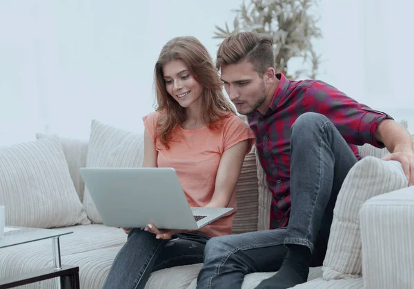 Młody człowiek z jego dziewczyna, patrząc na laptopie siedzi na kanapie. — Zdjęcie stockowe