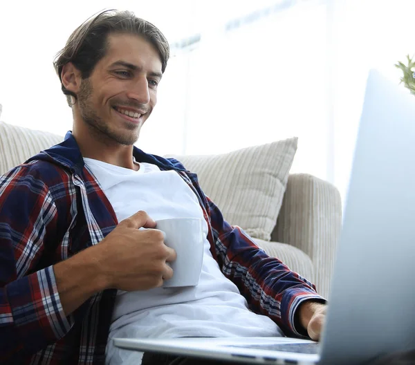 Junger Mann trinkt Tee auf dem Boden in der Nähe des Sofas. — Stockfoto