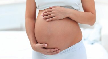 Hafif arka planda genç hamile bir kadının portresi.