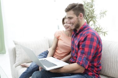 Genç çift kanepede oturan dizüstü bilgisayar ile gülümseyen