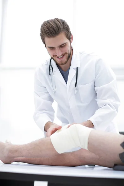 Smiling doctor looking at the bandage on the patients leg — Stock Photo, Image