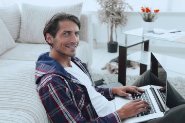 gülümseyen adam kanepede yakın katta oturan bir dizüstü bilgisayar ile