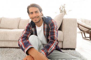 Kendine güvenen adam rahat bir oturma odasında halı üzerinde oturan.