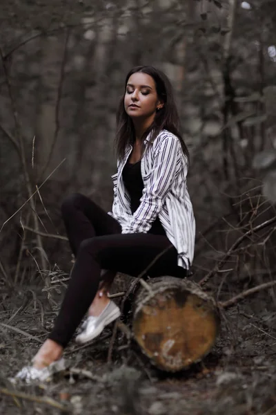 Mujer joven sentada en un tronco en el bosque . — Foto de Stock
