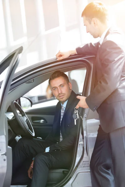 Erfolgreicher Geschäftsmann, der vom Verkäufer im Showroom die Autoschlüssel erhält — Stockfoto