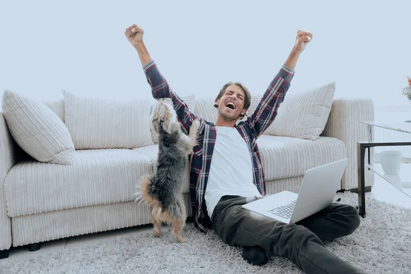 Glad ung man jublar med sin hund som sitter i vardagsrummet — Stockfoto