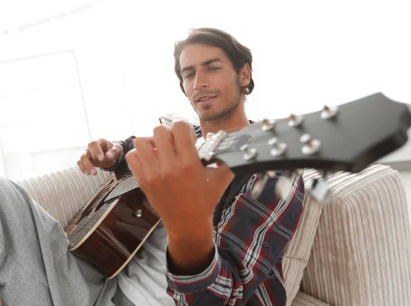 Um tipo com uma guitarra sentada no sofá na sala de estar. conceito de um estilo de vida — Fotografia de Stock