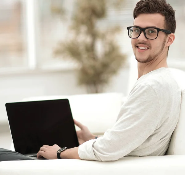 Jeune homme moderne travaillant sur ordinateur portable assis dans le salon . — Photo