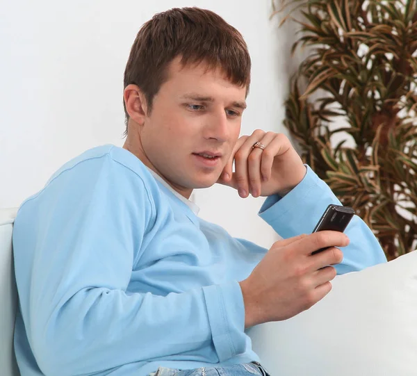Bilden av en ung man sitter i soffan och med en telefon — Stockfoto