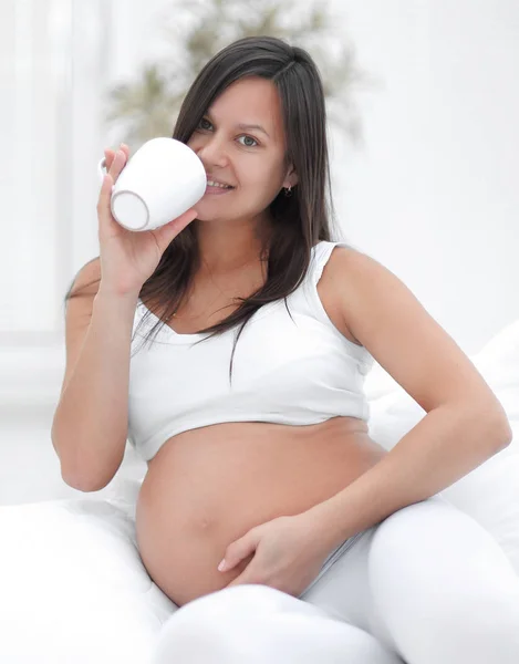 Glad gravid kvinna konsumtionsmjölk som sitter i vardagsrummet. — Stockfoto