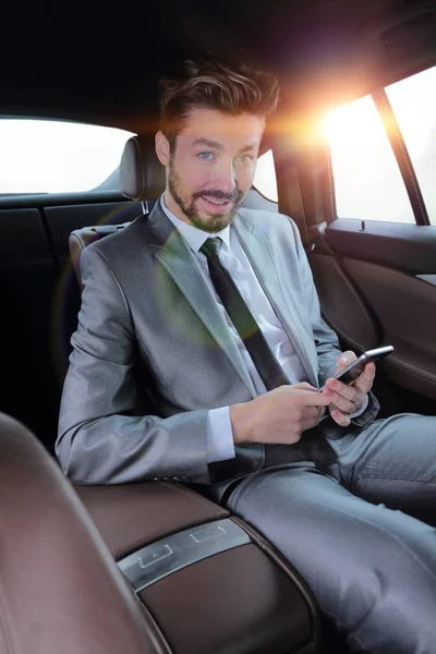Uomo in giacca e cravatta seduto in auto e leggere messaggi su smartphone — Foto Stock