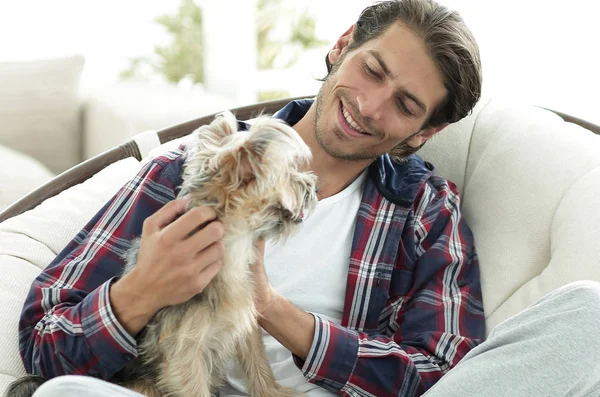 Chico guapo con un perro sentado en un sillón grande . — Foto de Stock