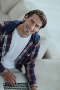 dizüstü bilgisayarda çalışan ve kameraya bakarak bir genç adam. Yukarıdan görüntülemek