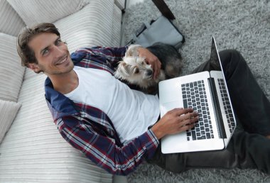 yakışıklı adam köpeğini sarılma ve kanepede oturan dizüstü bilgisayar ile