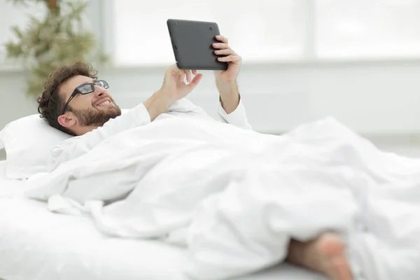 Schläfriger Mann blickt auf den Bildschirm eines digitalen Tablets. — Stockfoto
