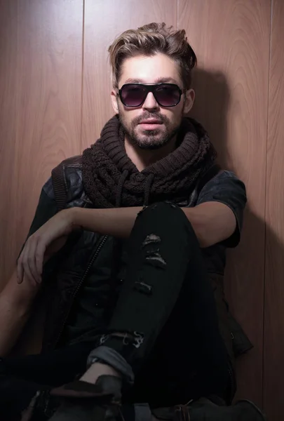 Hombre de moda relajado en gafas de sol se sienta en madera en el estudio — Foto de Stock