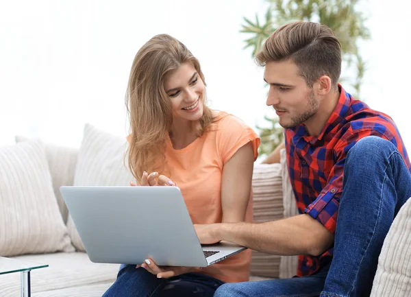 Young couple is using a laptop and smiling while sitting on sofa at home — Stock Photo, Image