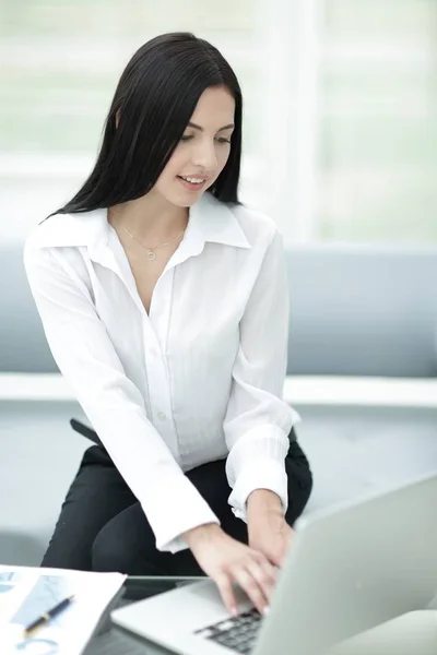 Framgångsrik ung kvinna sitter vid ett skrivbord på en suddig bakgrund. — Stockfoto