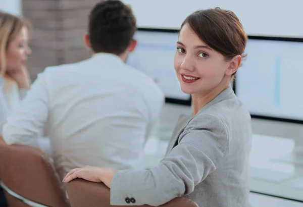 Vista trasera. hermosa mujer de negocios sentada cerca del escritorio y mirando a la cámara . — Foto de Stock