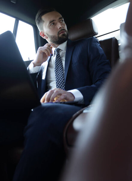 businessman working with laptop and looking out the window of a car