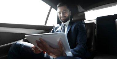 bir arabanın arka koltuğunda çalışma ve bir tablet kullanarak iş adamı
