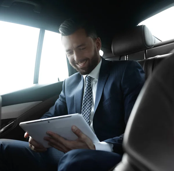 Podnikatel s digitálním tabletu sedí na zadním sedadle auta — Stock fotografie