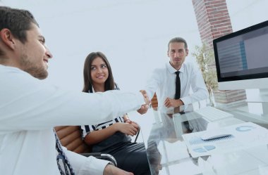 Erkekler masada otururken el sıkışıyor ve gülümsüyor.