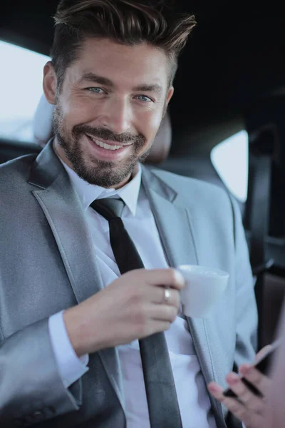 Podnikatel, pití kávy na zadním sedadle auta — Stock fotografie