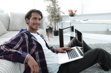 modern oturma odasında otururken dizüstü bilgisayar ile büyüleyici genç adam