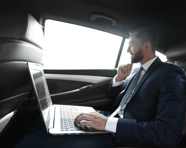 Empresario escribiendo texto en el ordenador portátil mientras está sentado en el coche —  Fotos de Stock