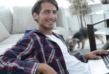 gülümseyen adam kanepede yakın katta oturan bir dizüstü bilgisayar ile