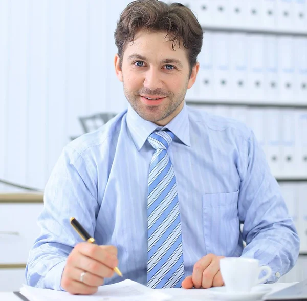 Primo piano bell'uomo d'affari che firma un documento, seduto dietro una scrivania — Foto Stock