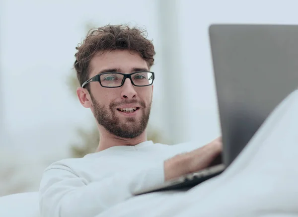 Χαμογελαστός άνθρωπος που χρησιμοποιούν φορητό υπολογιστή ξαπλωμένος στο κρεβάτι — Φωτογραφία Αρχείου