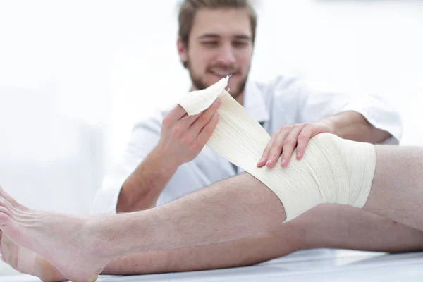 Médecin bandage d'une blessure sur la jambe du patient — Photo