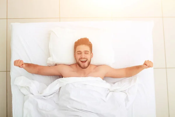 Pohled shora. šťastný muž, probuzení v pohodlné posteli — Stock fotografie