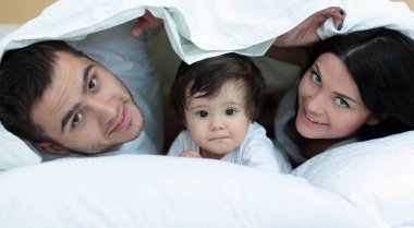 mutlu bir aile kameraya bakarken bir yorgan altında poz