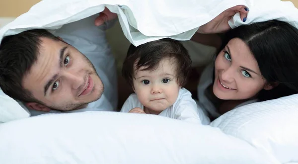 O familie fericită pozând sub o plapumă în timp ce se uită la cameră — Fotografie, imagine de stoc